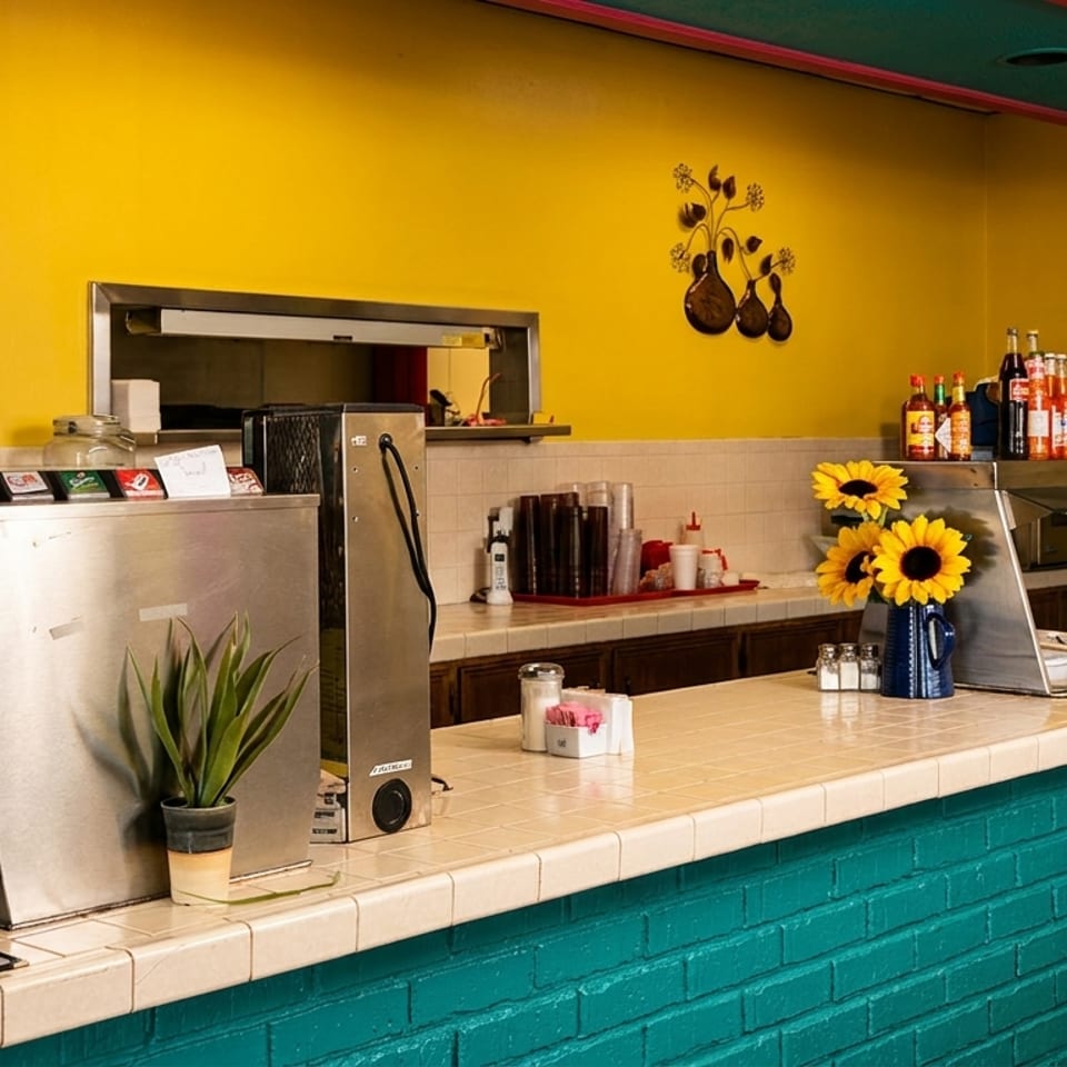 A vibrant yellow and teal restaurant counter with coffee makers, a buffet, and sunflowers.
