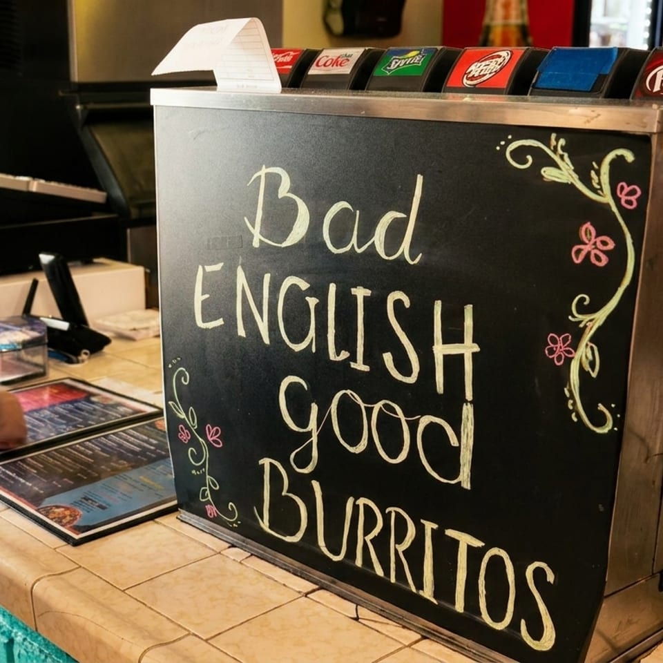 A chalkboard sign reads "Bad English, good Burritos" next to a soda fountain and restaurant counter.